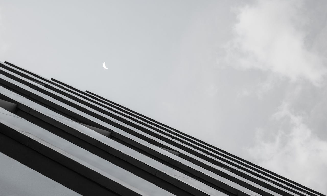 A low angle view of a modern skyscraper against a sky with a visible half-moon in Santiago de Compostela, Spain.